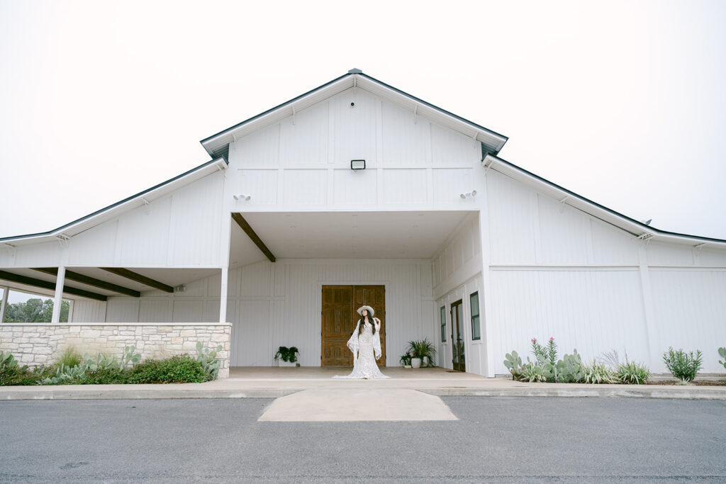 Bride walking from covered portico at The Videre’s stables in a lace gown and cowboy hat