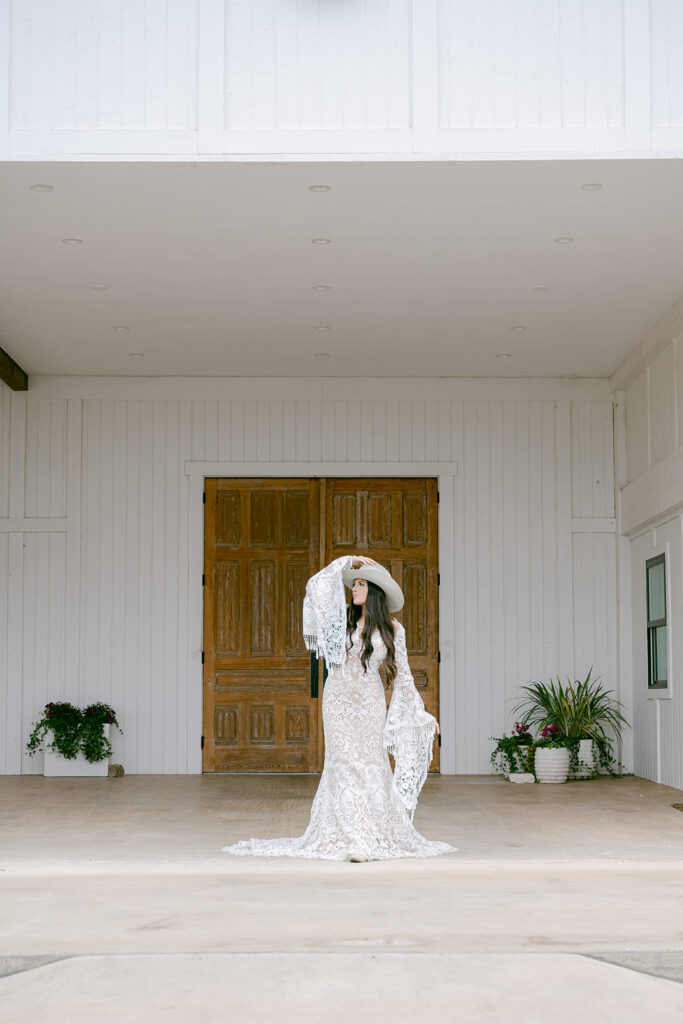 Bride in lace gown standing under covered entry to The Videre’s renovated stables