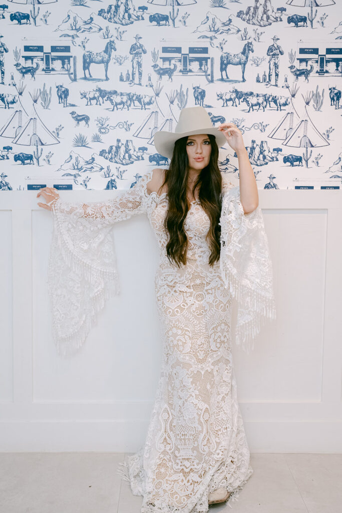 Bride in western lace dress and hat posing in front of navy and white Texas-themed wallpaper at The Videre