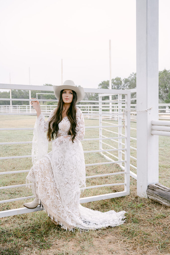 Bride in lace gown seated along fence rail at The Videre’s open-air arena