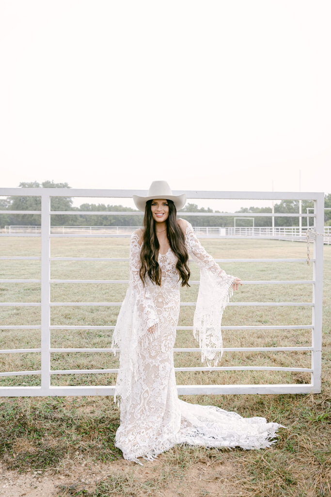 Bride smiling at camera near white ranch fence at The Videre’s open field arena