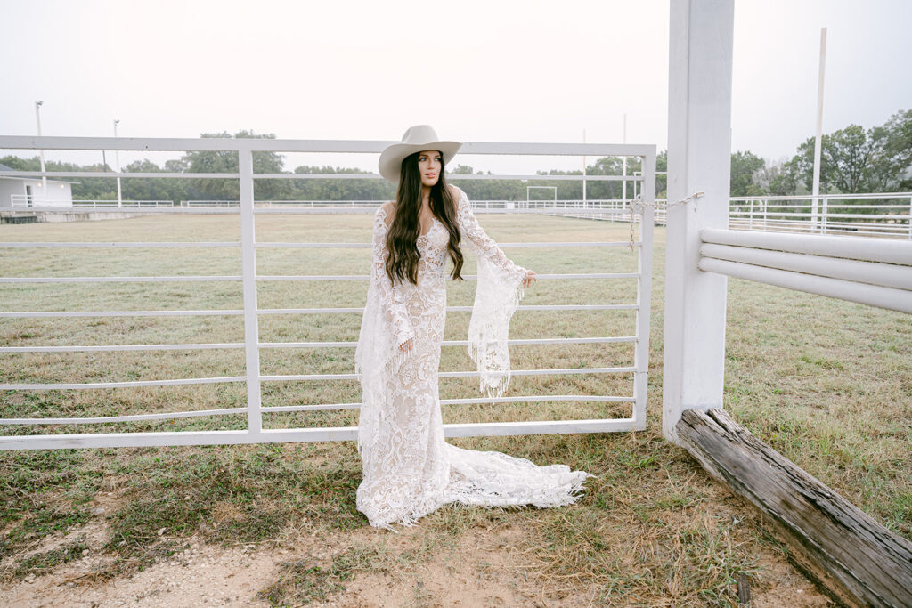 Bride standing confidently with one hand on hat inside fenced field at The Videre