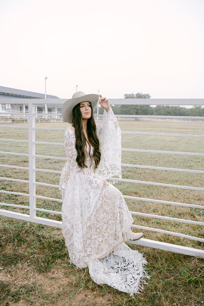 Bride standing against arena fencing at The Videre with soft pink sky at sunset