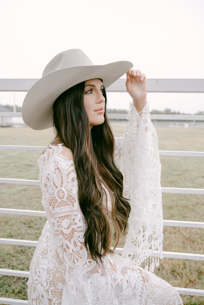 Close-up of bride in hat holding fence post and smiling at The Videre wedding venue