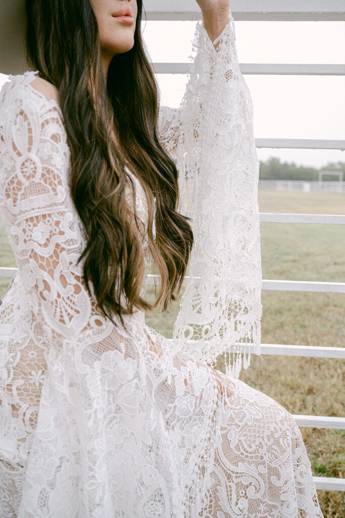 Detail of bride’s lace sleeve and long curls against white ranch rail at The Videre