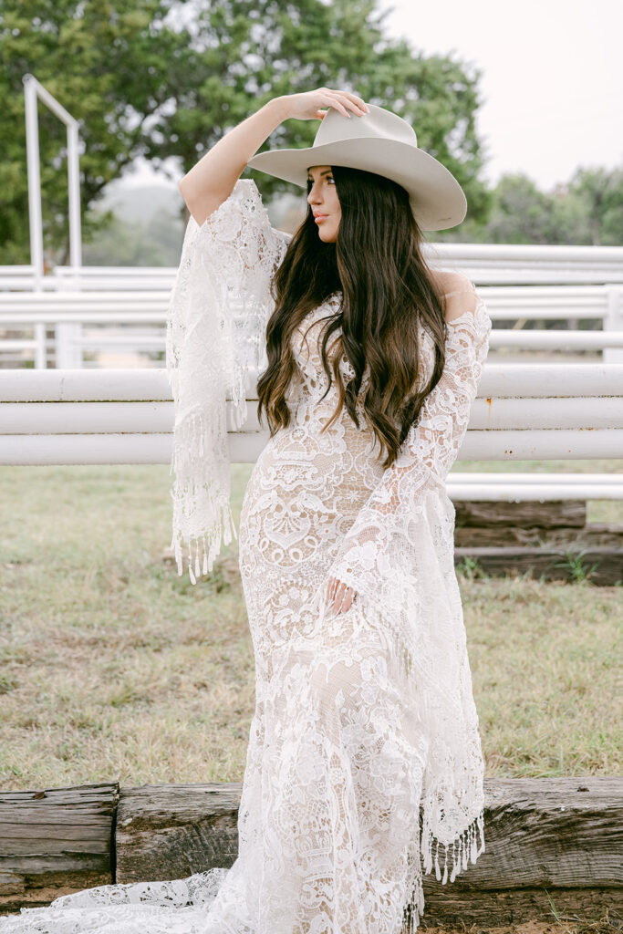Bride adjusting hat near arena rail in western lace gown at The Videre wedding venue