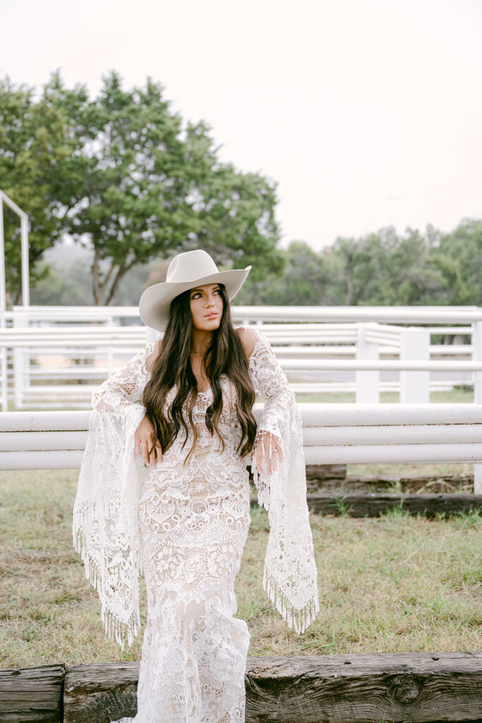 Bride walking through arena in lace gown and cowboy hat at The Videre wedding venue