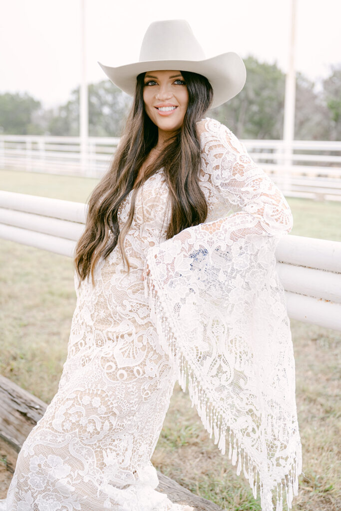 Bride smiling in profile with white cowboy hat and lace gown at The Videre wedding arena