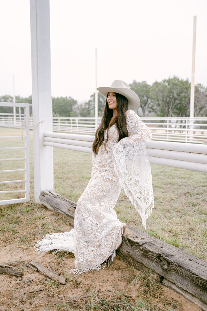 Bride pausing at white arena gate in long lace gown at The Videre wedding venue