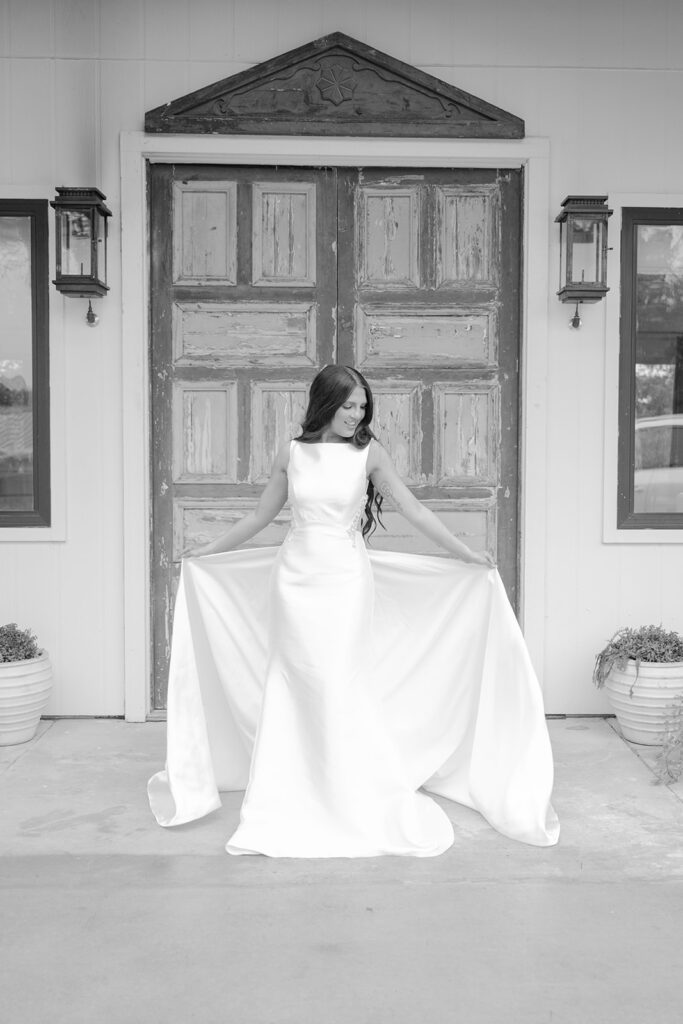 Bride holding gown in both hands in front of The Château at The Videre, black and white edit