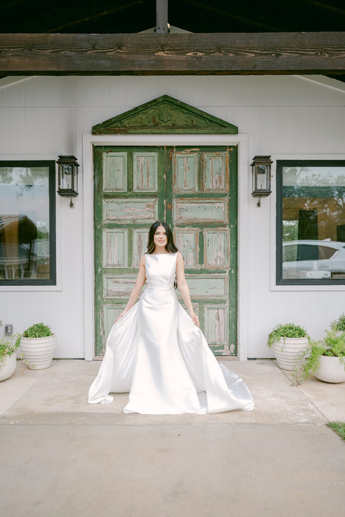 Bride standing in front of vintage green doors at The Videre’s bridal Chateau in a classic designer white gown