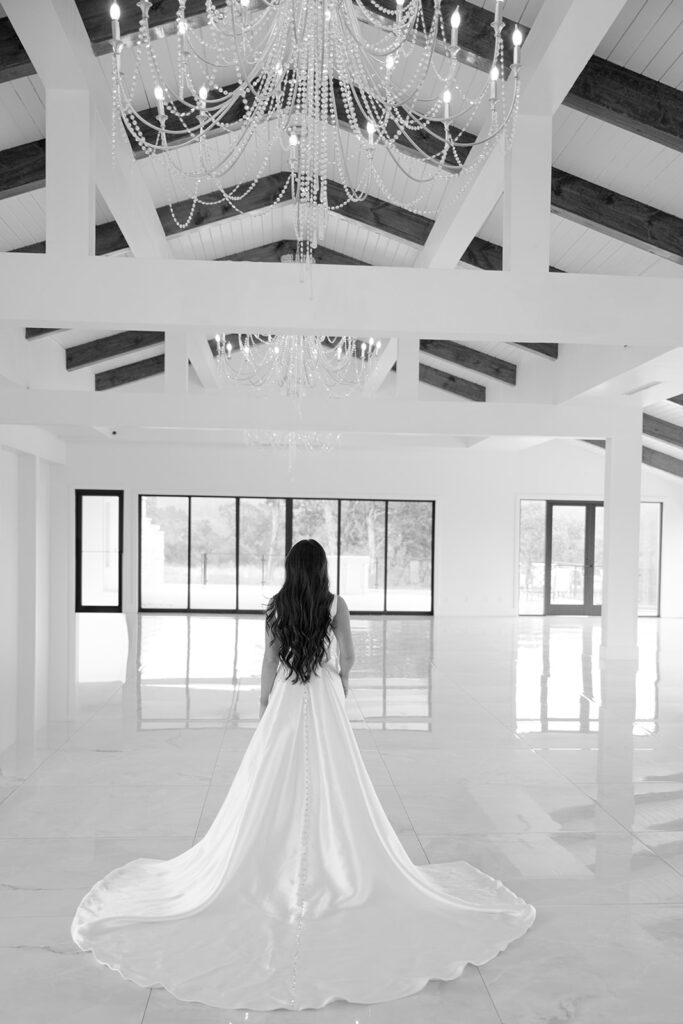 Bride standing under chandeliers at The Videre wedding venue with chapel-style ceiling beams