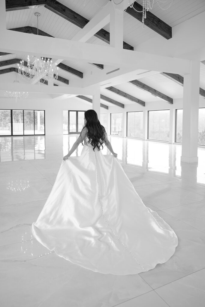 Bride walking across chandelier-lit white hall at The Videre with large windows behind