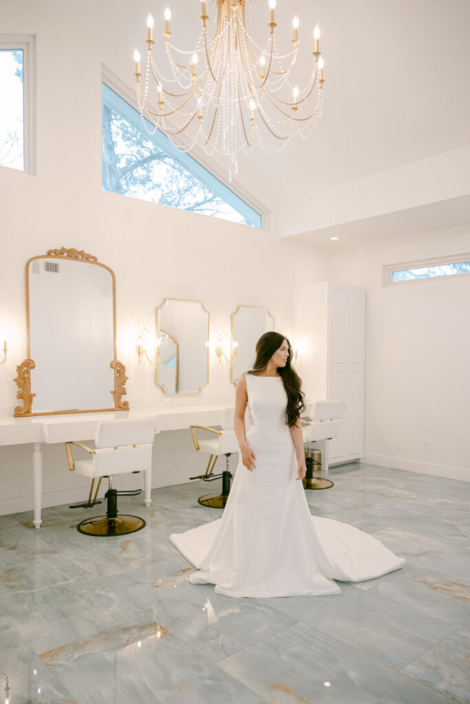Bride standing under chandelier inside The Château’s getting-ready suite at The Videre wedding venue