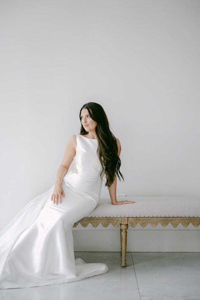 Bride in modern satin gown looking off-camera while seated on bench at The Videre wedding venue
