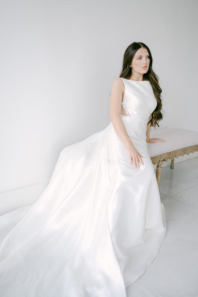 Bride seated and gazing forward in structured satin gown inside The Videre wedding venue