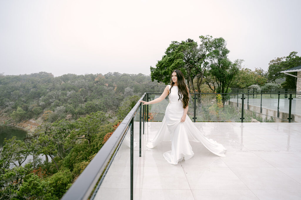 Bride holding railing at The Videre wedding venue with lush hill country view behind her