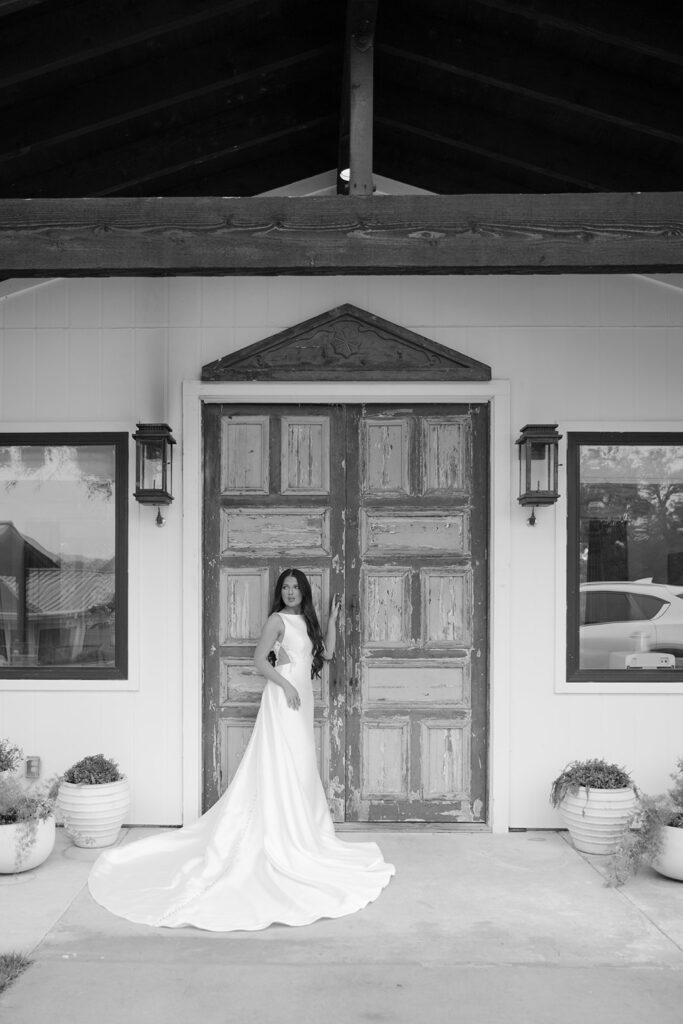 Black and white image of bride in front of green antique doors at The Château at The Videre wedding venue