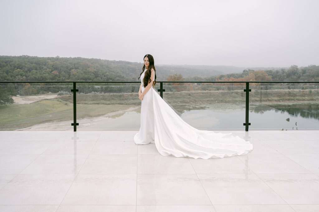 Bride with long train standing at the glass terrace of The Videre wedding venue in Texas.