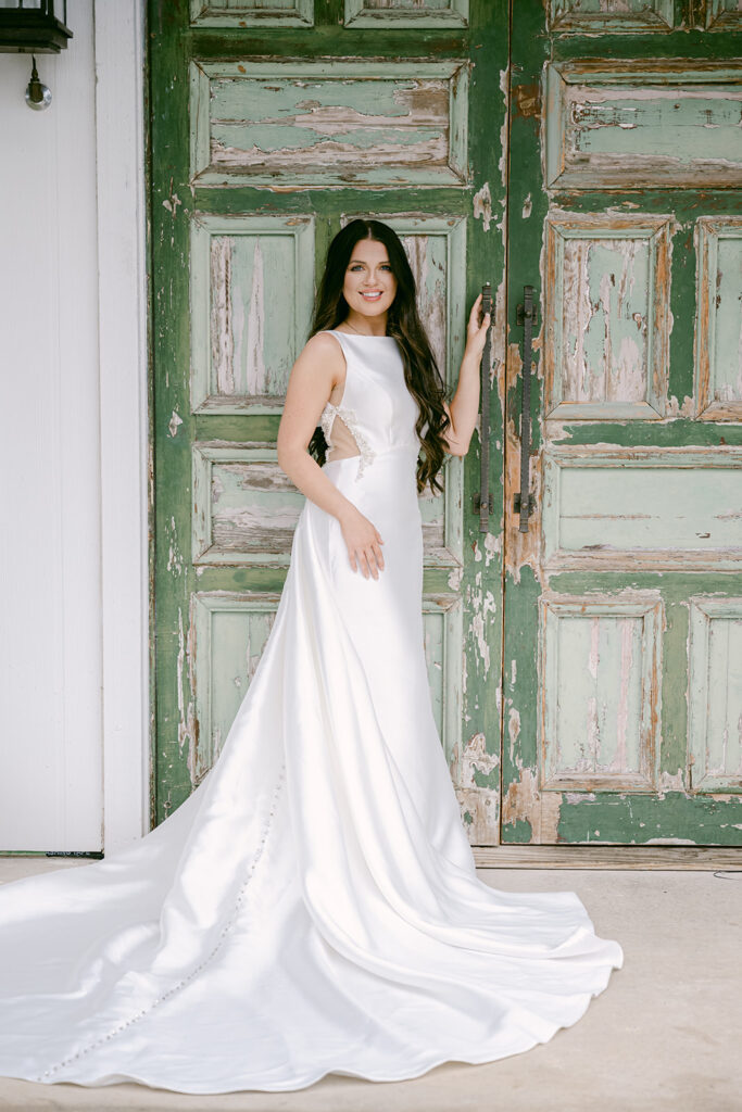 Bride smiling and leaning against antique green doors at The Château at The Videre wedding venue