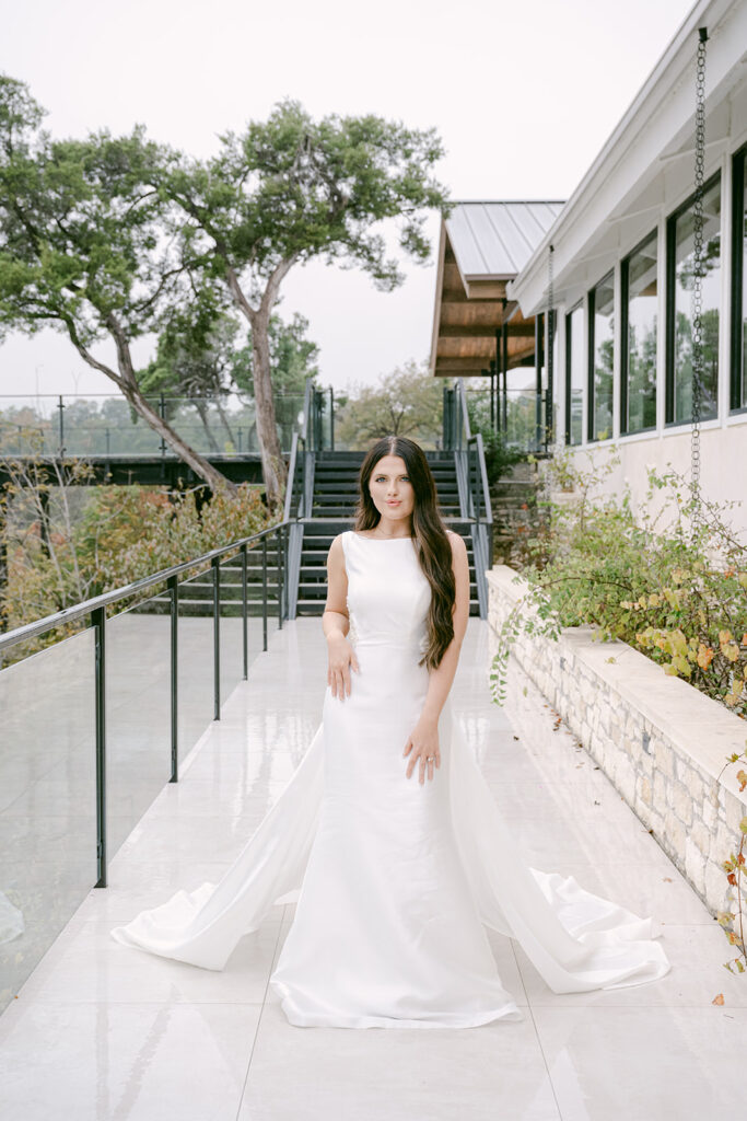 Bride facing camera and resting arms on stone wall along garden path at The Videre wedding venue