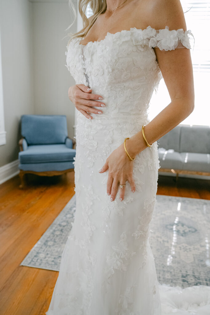 Bride in off-the-shoulder gown holding her stomach in a quiet moment at The Allen Farmhaus