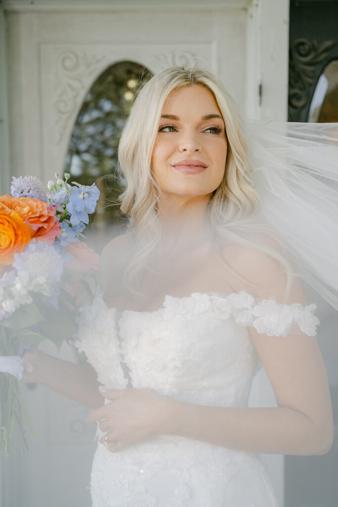 Bride holding bouquet and smiling with veil softly blowing across her face at The Allen Farmhaus