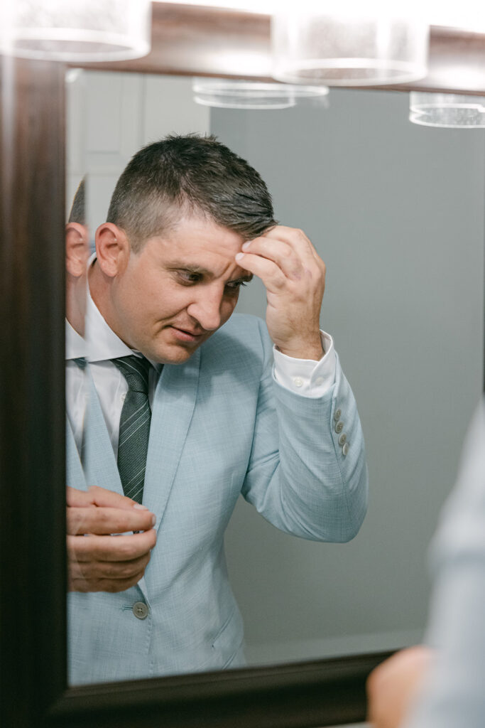Groom getting ready and adjusting hair in mirror at The Allen Farmhaus