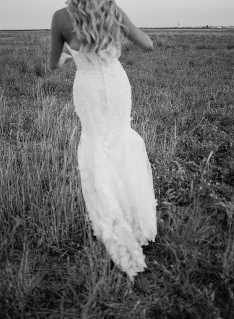 Bride walking through open Texas field in black and white film photo at The Allen Farmhaus