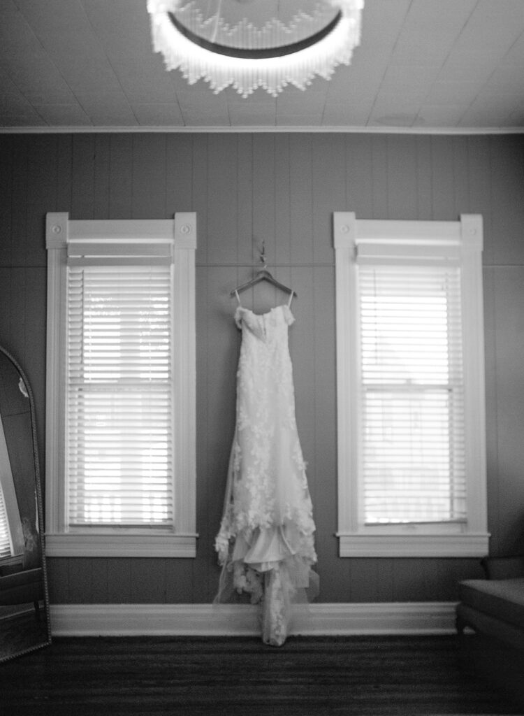 Bridal gown hanging in window-lit prep space at The Allen Farmhaus, photographed on black and white film