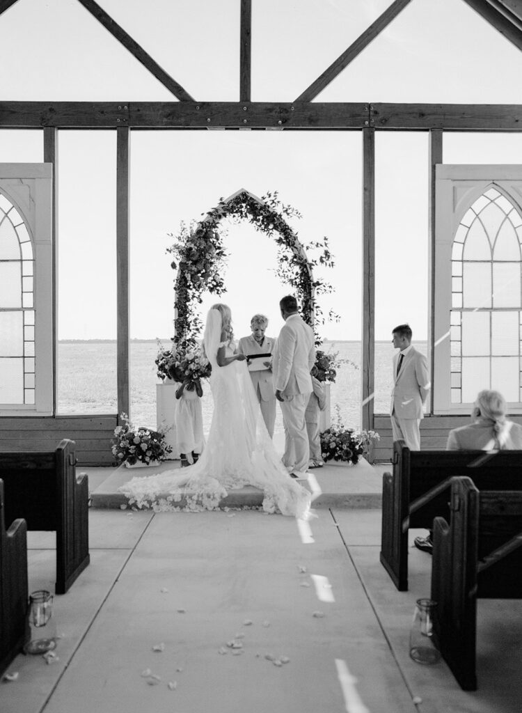 Couple at the altar framed by arch during ceremony at The Allen Farmhaus, photographed on film